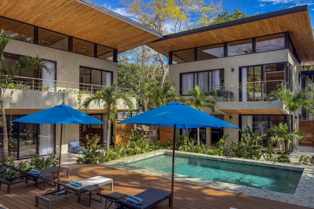 Piscina compartida de Nori Villas con sombrillas azules y deck de madera