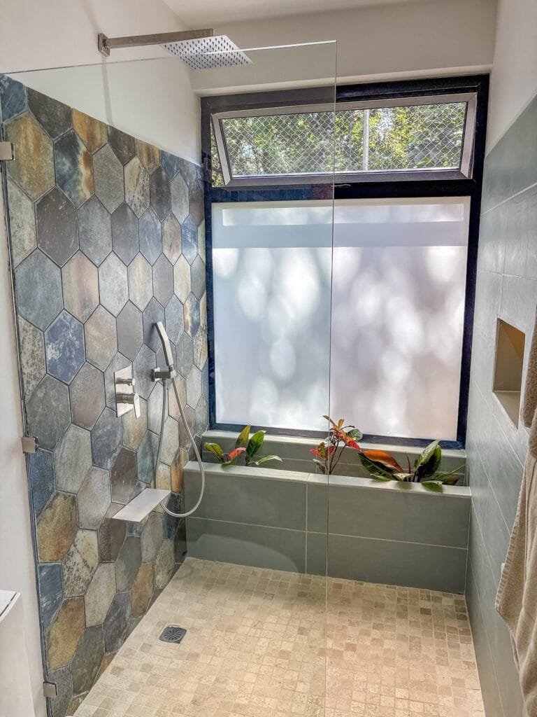 Ducha a ras de piso del apartamento Perico con pared de piedra hexagonal y plantas